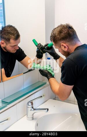 A professional cleaner scraping dirt and spots from a bathroom mirror during a general spring cleaning of an apartment bathroom Stock Photo