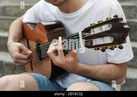Young man sits on the steps and play on guitar Stock Photo
