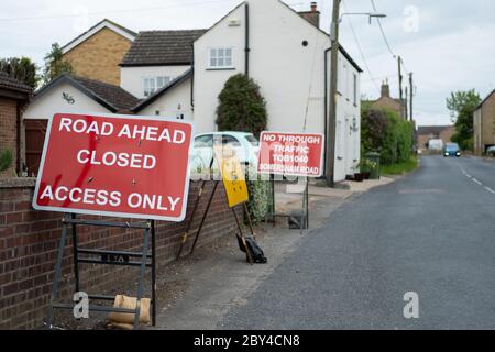 Multiple road traffic warning signs seen located near rural houses in a village setting.