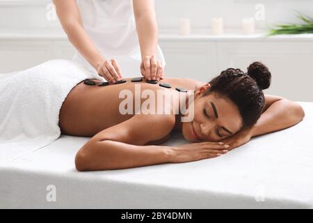 Relaxed african woman getting hot stone massage at spa Stock Photo