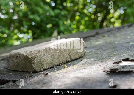 Heavy paving stone seen laid on an old shed roof following high wind which has partially removed the asphalt roof lining. Stock Photo