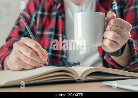 Freelancer writing notes and drinking coffee in home office while working from home, selective focus Stock Photo