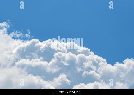 Cumulus cloud relief on a smooth background of clear summer sky. Upper part of white fluffy cloud against blue sky on a sunny day. Close-up. Stock Photo