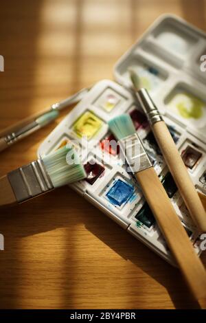 Different brushes for painting and watercolor paints in a white box on a wooden table. Stock Photo