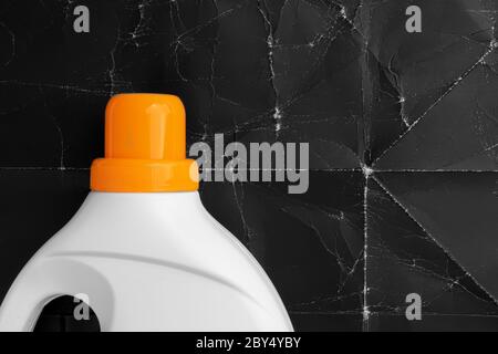 Laundry detergent in a plastic white container with a bright orange screw cap on a background of old crumpled black paper. Recovery and cleaning conce Stock Photo