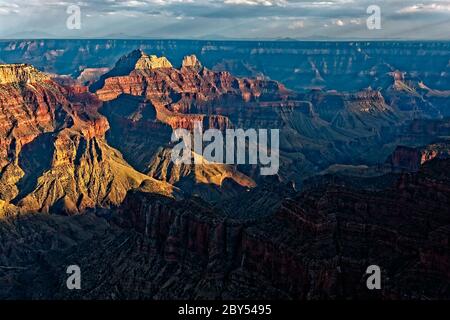 A casts dark shadows over the Grand Canyon. In the distance streaks of rain come from dark clouds Stock Photo