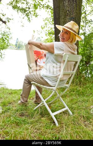 Elderly woman paints picture with water colors in nature in summer Stock Photo