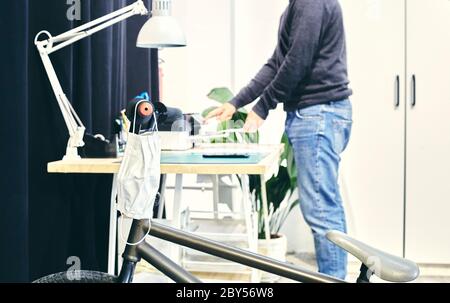 Bicycle parked with a mask hanging from the handlebars in the foreground with a person in the background in the printer section of a coworking Stock Photo