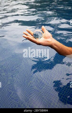 An Human hand holding a glass ball over the water