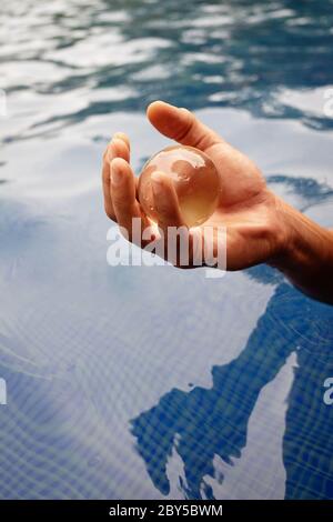 An Human hand holding a glass ball over the water