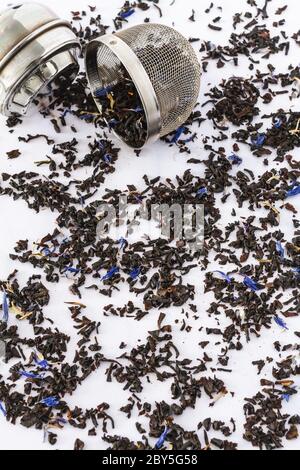 Earl grey and blue flowers with tea strainer on a white marble backdrop Stock Photo