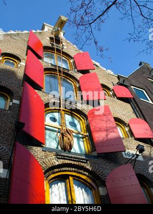 Amsterdam house with red window shutters and rope hanging on the hook, Netherlands Stock Photo