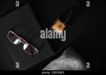 glasses,book, extinguished candle on a black background. Home,lifestyle concept. Stock Photo