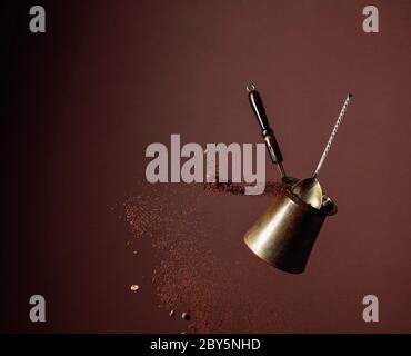 Old copper coffee maker and a spoon with ground coffee in motion. Spilled coffee ground and beans in motion. Brown background. Stock Photo