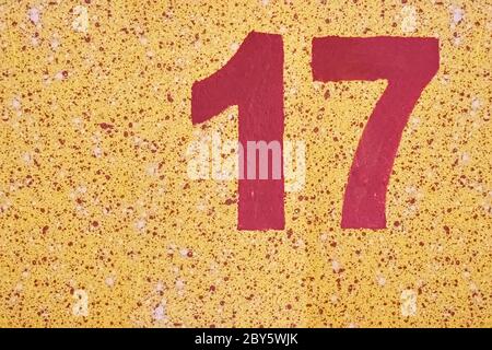 Number seventeen red color painted on a yellow wall with splashes. Stock Photo