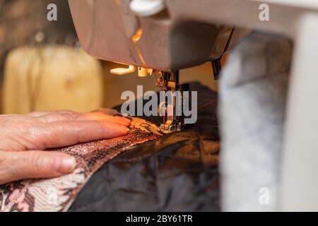 a close-up view of sewing process, hand of old woman using sewing machine, selective focus technique Stock Photo