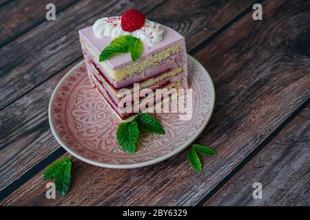 Tasty piece of raspberry multi-layered cake on plate. raspberry cake served for dessert on wooden background with mint leaves. Delicious slice tart on plate. Baking and decorating raspberry cake Stock Photo