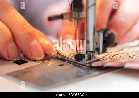 a close-up view of sewing process, hand of old woman using sewing machine, selective focus technique Stock Photo