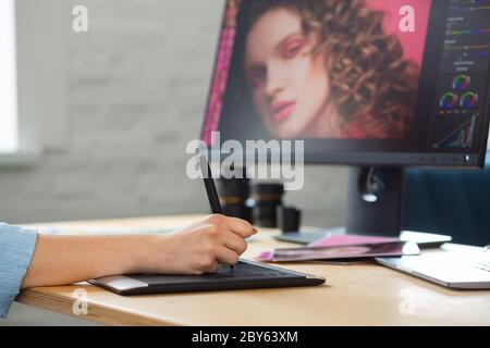 Close up portrait of graphic designer hands retouching images using graphic drawing tablet in special program. Laptop,monitor, and color palette Stock Photo