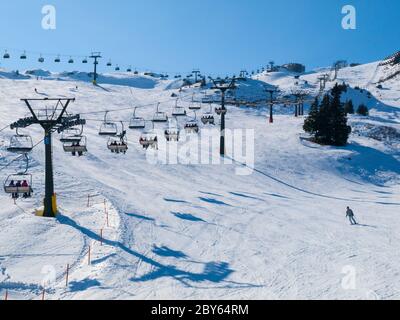 Ski lift and ski slope with skiers under it on sunny winter day with blue sky. Alpine resort Silvretta Arena near Samnaun and Ischgl, Switzerland and Austria, Alps, Europe Stock Photo