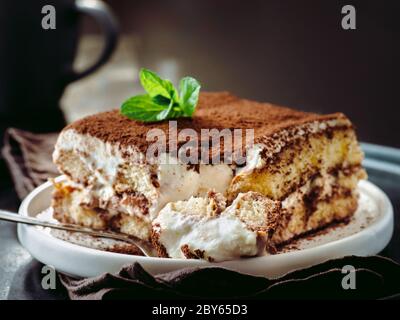 Perfect homemade tiramisu cake in spoon. Tiramisu portion on plate over dark tabletop background. Delicious no bake tiramisu ready-to-eat. Close up Stock Photo