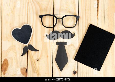 Happy Father Day background concept with glasses, blackboard, black heart shape, tie and black mustache on wooden background with copy space for text. Stock Photo