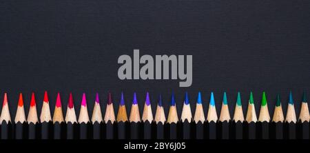 Creative minimal banner. Colored pencil set arranged in line on black background. Stock Photo
