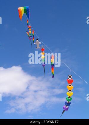 A collection of multi colored kites against a bright blue sky.