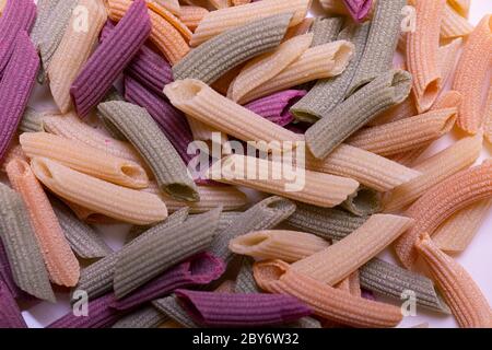 Tri-color penne pasta. Tomato, spinach and wheat pastas. Multicolored pasta of red, yellow and green color, organic square background. Stock Photo