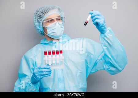 Photo of guy expert doc virologist hold sick patients blood probe tubes examining results watch one flask wear mask hazmat blue uniform surgical cap Stock Photo