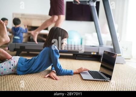 Girl using laptop on floor next to father on treadmill Stock Photo