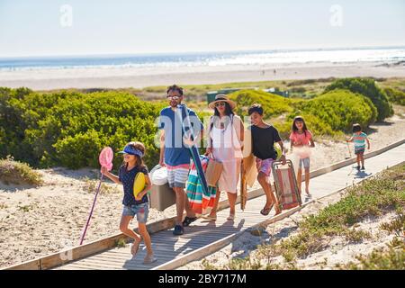 Family carrying chairs and toys on sunny beach boardwalk