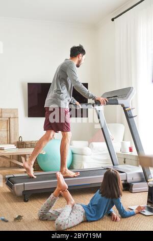 Daughter using laptop next to father on treadmill Stock Photo
