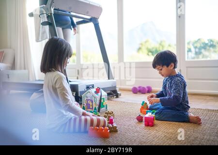 Kids playing with toys on floor by mother on treadmill Stock Photo