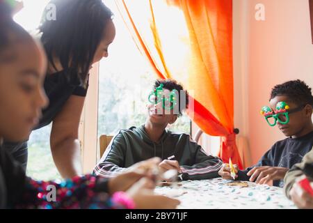 Mother and sons in Christmas glasses decorating cookies at table Stock Photo