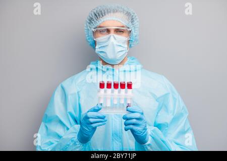 Photo of guy expert doc virologist hold sick covid patients blood probe tubes examining results wear mask hazmat blue uniform surgical cap suit Stock Photo