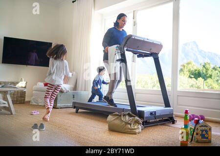 Kids running around mother exercising on treadmill Stock Photo