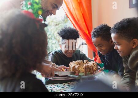 Father serving Christmas cake to eager sons at table Stock Photo