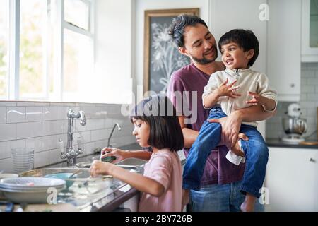 Happy father and kids doing dishes at kitchen sink