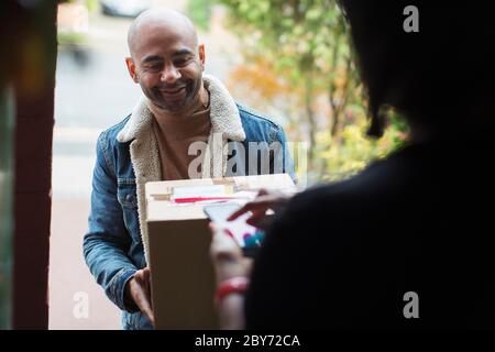 Delivery man delivering package to woman at front door Stock Photo