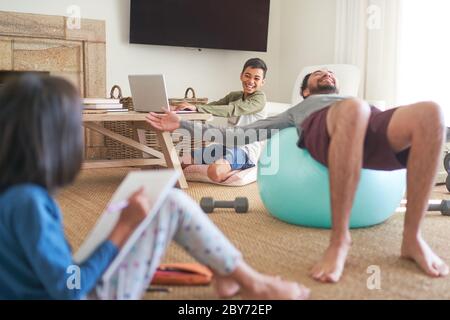 Happy father and kids exercising and doing homework in living room