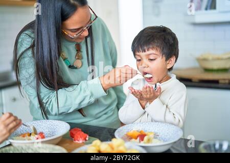 Mother feeding son in kitchen Stock Photo