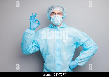 Photo of confident guy expert virologist doc center clinic professional showing okey symbol patient wear mask hazmat blue uniform suit plastic facial Stock Photo