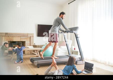 Father exercising on treadmill in living room with kids