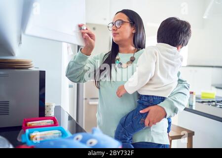 Mother holding son and preparing lunches in kitchen Stock Photo