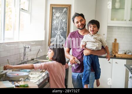 Portrait happy father and kids doing dishes in kitchen