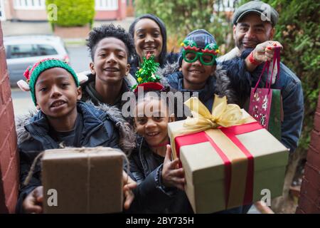 Portrait happy family arriving with Christmas gifts at front door Stock Photo