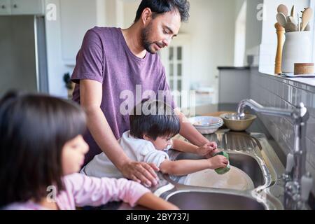 Father and kids doing dishes at kitchen sink Stock Photo