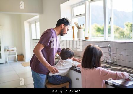 Father and kids doing dishes at kitchen sink