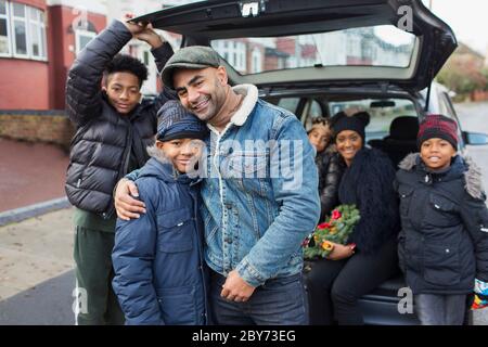 Portrait happy family hugging at back of car Stock Photo